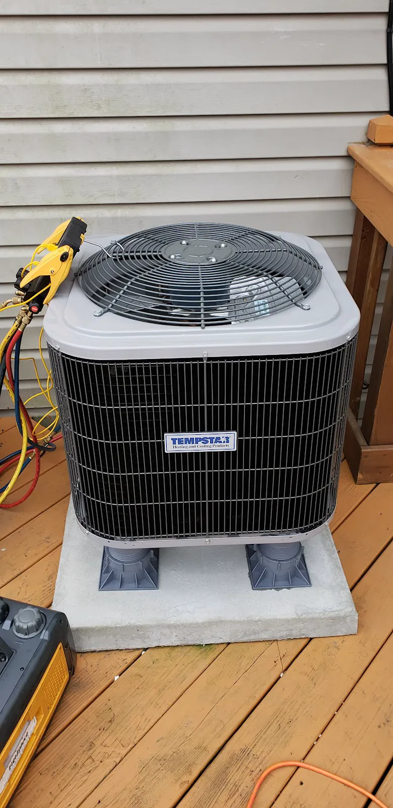 A Tempstar outdoor condenser on a pad on a wooden deck with refrigerant gauge hoses attached