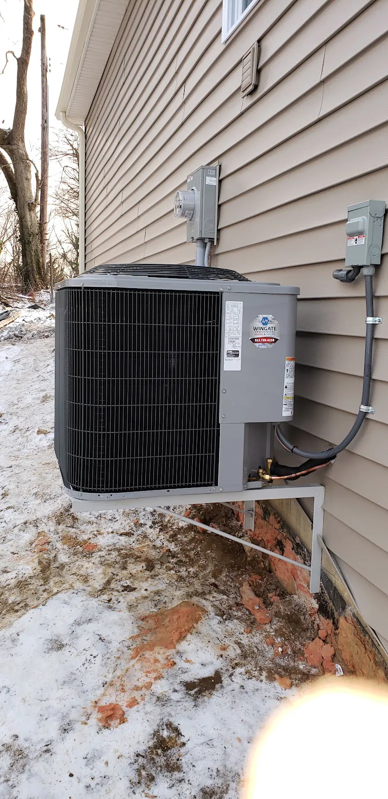 An outdoor unit on a wall bracket beside vinyl siding with snow on the ground