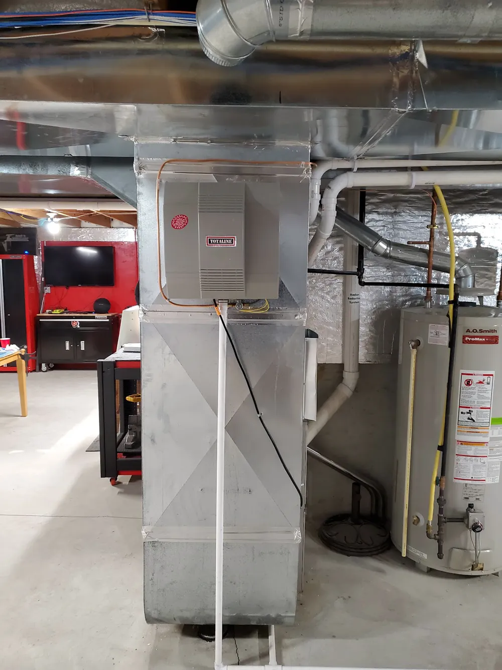 A basement furnace with a whole-house humidifier mounted on the supply duct, next to a water heater